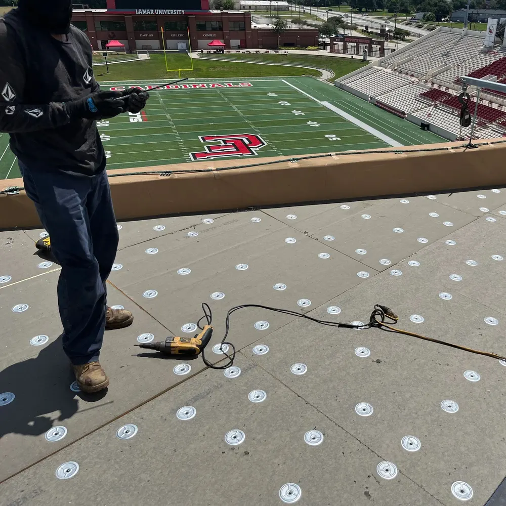 Roofing work in progress overlooking a stadium, with a worker and tools on the roof